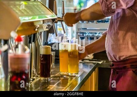Un employé sert trois bières de teintes différentes au comptoir de la brasserie artisanale Pfefferlechner à Lana, dans le Tyrol du Sud, en Italie ; un verre de « Pfeffer Schwarz » sombre est déjà prêt. La brasserie artisanale de la famille Laimer, en activité depuis 2005, brasse plusieurs variétés, de « Pfeffer Hell » à « Pfeffer Schwarz » et de la bière aux châtaignes à la pale ale ; sa dernière création est une bière sans alcool, que la famille Laimer affirme être la première du Tyrol du Sud. Banque D'Images