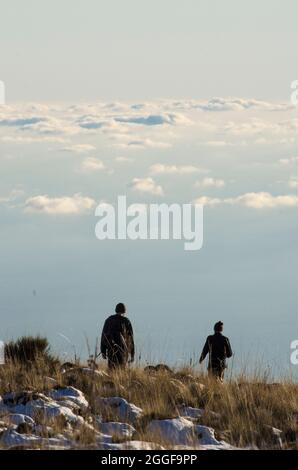 deux hommes avec sac à dos marchant dans un paysage de haute montagne enneigé, il est au-dessus des nuages Banque D'Images