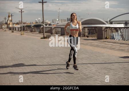 Femme en vêtements de sport et baskets court le long du front de mer vide de la ville Banque D'Images