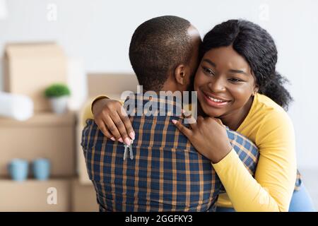 Notre maison Fists. Joyeuse femme afro-américaine tenant les clés de la maison et embrassant son mari, heureux conjoints noirs célébrant l'achat de propriété et de déménagement à Banque D'Images