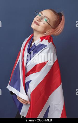 Jeune femme expatrié à lunettes avec le drapeau de la Grande-bretagne. Prise de vue en studio. Enseignant de hippster anglais. Fashionly habit la femme avec des poils roses en noir Banque D'Images