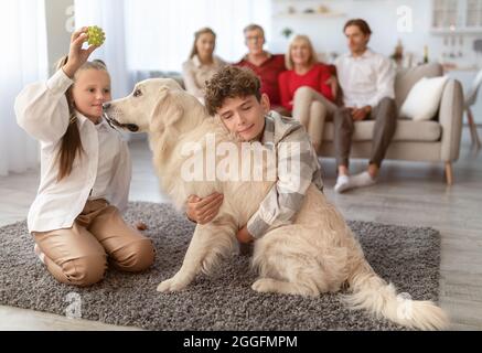 Adorables enfants jouant et embrassant chien d'animal de compagnie pendant que leur grande famille se détend sur le canapé dans le salon. Les enfants s'amusent avec Golden Retriever au rez-de-chaussée A. Banque D'Images