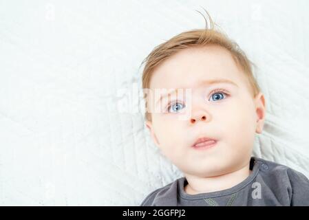 Portrait de tête de bébé mignon garçon allongé sur le lit, montre la langue. Copier l'espace Banque D'Images