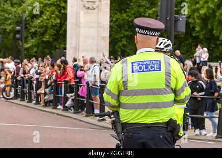 Londres, Angleterre - août 2021 : vue arrière d'un officier de police métropolitain portant une veste réfléchissante. En arrière-plan se trouvent des foules de personnes. Banque D'Images