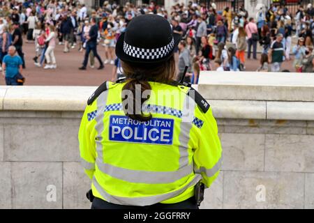 Londres, Angleterre - août 2021 : vue arrière d'un officier de police métropolitain portant une veste réfléchissante. En arrière-plan se trouvent des foules de personnes. Banque D'Images