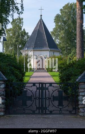 Helsinki / Finlande - 28 AOÛT 2021 : fermeture d'une porte en fer au cimetière avec une route en terre menant à une petite chapelle en arrière-plan. Banque D'Images