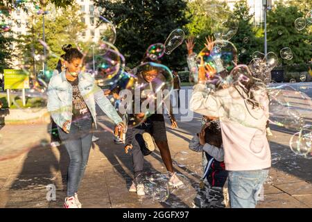 Les familles apprécient les divertissements de la rue le long de la Southbank à Londres tandis qu'un interprète souffle de grandes bulles à travers le pavé, Angleterre, Royaume-Uni. Banque D'Images