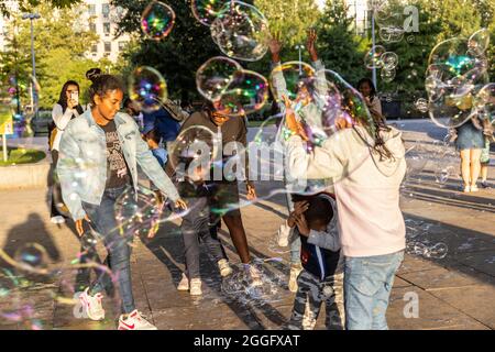 Les familles apprécient les divertissements de la rue le long de la Southbank à Londres tandis qu'un interprète souffle de grandes bulles à travers le pavé, Angleterre, Royaume-Uni. Banque D'Images