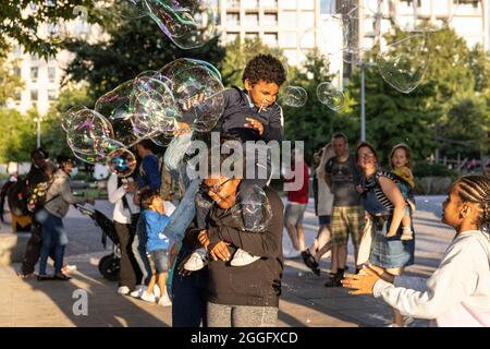 Les familles apprécient les divertissements de la rue le long de la Southbank à Londres tandis qu'un interprète souffle de grandes bulles à travers le pavé, Angleterre, Royaume-Uni. Banque D'Images