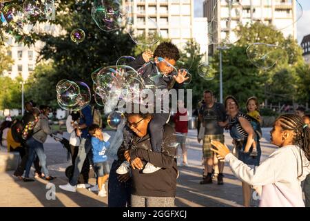 Les familles apprécient les divertissements de la rue le long de la Southbank à Londres tandis qu'un interprète souffle de grandes bulles à travers le pavé, Angleterre, Royaume-Uni. Banque D'Images