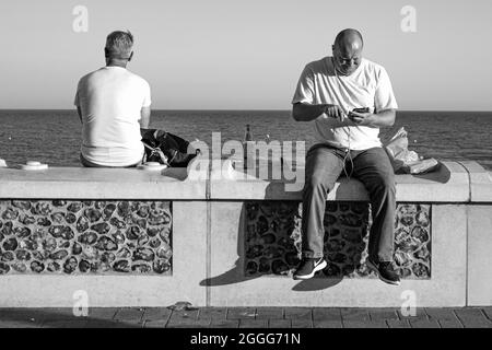 BRIGHTON, ROYAUME-UNI - 03 juillet 2021 : une photo en échelle de gris de deux hommes assis sur une clôture sur la mer à Brighton, au Royaume-Uni Banque D'Images