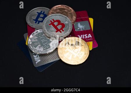 Plusieurs pièces de monnaie en Bitcoin brillantes, avec CARTES DE débit et de crédit VISA sur un fond sombre. Monnaie virtuelle électronique BTC. Banque D'Images