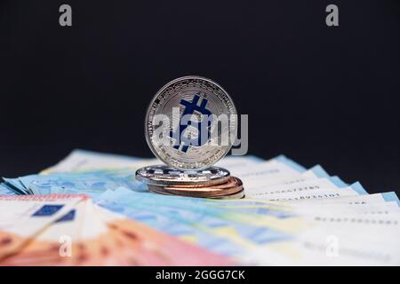 Les bitcoins avec le symbole bleu en évidence se trouvent au-dessus des billets de banque de 20 et 10 euros. Bitcoins sur des billets de dix et vingt euros sur fond sombre. Banque D'Images