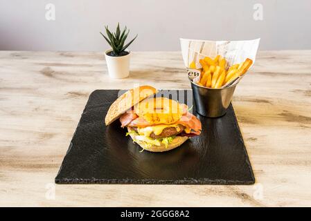 Hamburger hawaïen avec beaucoup de bacon, steak de bœuf, laitue, tranches d'ananas et crème de cheddar avec frites Banque D'Images