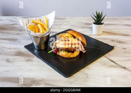 Hamburger de bœuf avec fromage cheddar double et nuggets, bacon frit et laitue garnie de frites sur une table en bois Banque D'Images