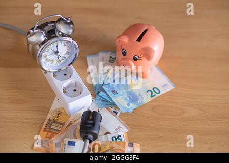 piggy bank avec billets en euros sur la table et prises électriques et une horloge analogique. Banque D'Images