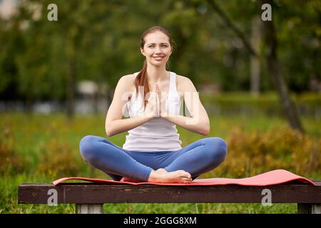 Femme souriante sur le banc du parc fait des exercices de yoga. Banque D'Images