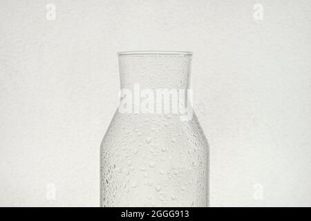 Demi-bouteille en verre transparent rétroéclairé et gouttes d'eau sur sa surface avec fond blanc. Banque D'Images