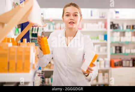 Portrait de diligent souriant agréable positive femme buveuse en manteau blanc travaillant en pharmacie Banque D'Images