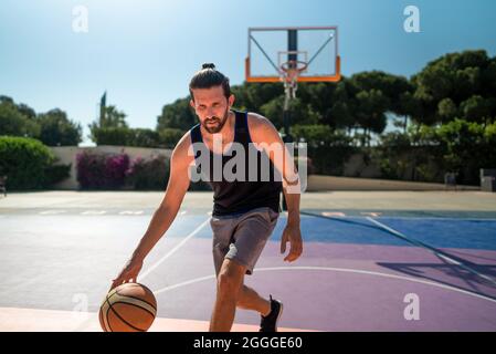 FIT homme jouant au basket-ball extérieur, temps ensoleillé, terrain de jeu moderne. Prise de vue à lentille large Banque D'Images