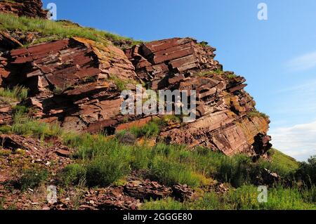 Une formation de roche en couches de couleur rouge vif, surcultivée avec de l'herbe basse au sommet d'une colline élevée. Coffres de montagne, Khakassia, Sibérie, Russie. Banque D'Images