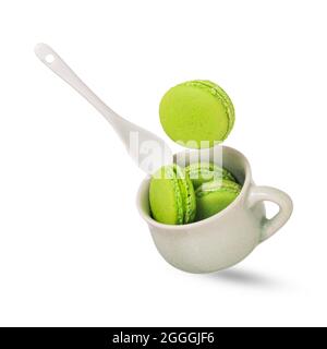 Un morceau de macaron vert pistache ou de macarons français tombant sur une tasse de céramique vert tendre remplie de macarons. Banque D'Images