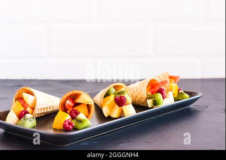 couper les fruits mûrs dans des cornets de gaufres sur le bleu. sur une table noire contre un mur de briques blanches Banque D'Images