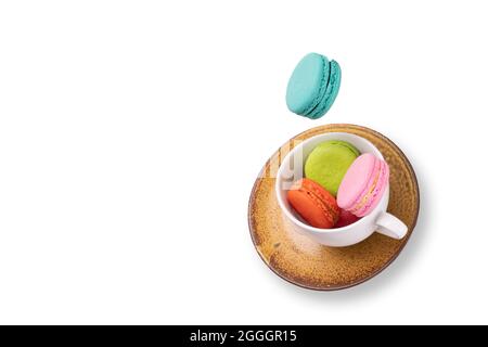 Macarons colorés flottant sur une tasse de thé blanc et une assiette en céramique orange. Isolation sur fond blanc. Concept de lévitation alimentaire. Banque D'Images