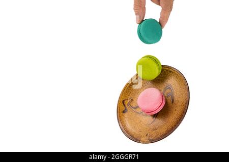 Des macarons colorés se levent sur une soucoupe tombant avec une main tenant l'un des biscuits. Isolation sur fond blanc Banque D'Images