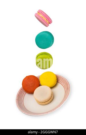 Macarons colorés flottant sur une soucoupe en céramique. Isolation sur fond blanc. Concept de lévitation alimentaire. Banque D'Images