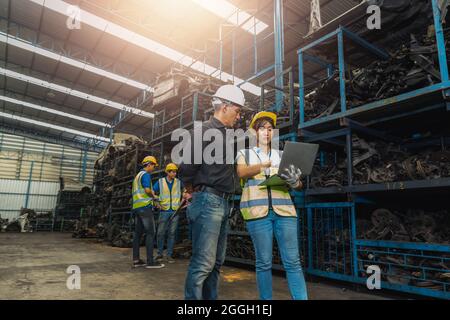 Le contrôleur de l'ingénieur vérifie et parle avec un ingénieur travaillant sur l'ordinateur portable en usine de pièces de rechange automobiles anciennes Banque D'Images