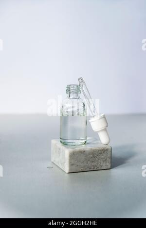 Bouteille de sérum cosmétique avec pipette sur podium sur fond gris clair. Produits d'autosoin tendance. Vue avant. Banque D'Images