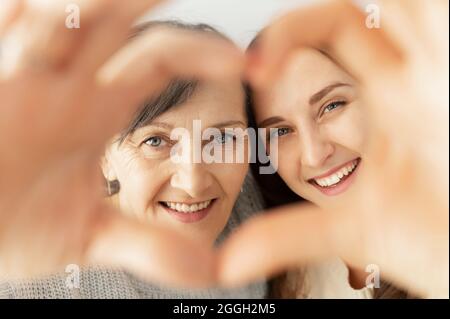 Portrait en gros plan de la belle mère âgée et de la fille adulte regarder l'appareil photo à travers le coeur des paumes, le cadre en forme de coeur, heureux mère à la retraite et fille adulte rire Banque D'Images