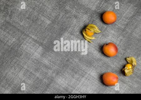 Les abricots et les physalis frais mûrs sont sur un tissu texturé gris. Alimentation saine. Vue de dessus. Gros plan. Copier l'espace. Mise au point sélective. Banque D'Images