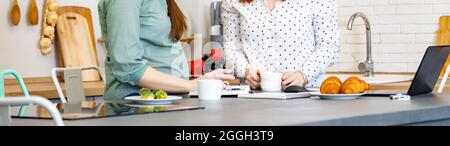 Banner, deux jeunes femmes qui parlent avec enthousiasme dans un café tout en travaillant sur des ordinateurs portables et en buvant du thé. Femmes enceintes qui parlent de la parentalité Banque D'Images