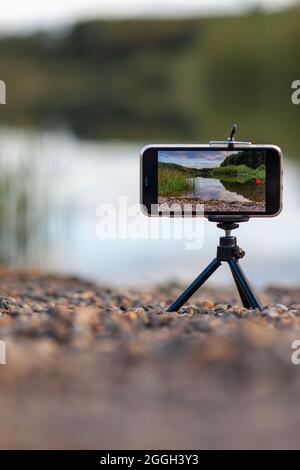 Un gros plan du téléphone sur un trépied prend une vidéo ou une photo de la nature. Un beau lac dans la forêt avec des nuages dans l'écran du photographe Banque D'Images