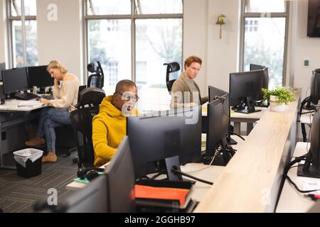 Divers collègues masculins et féminins au travail, assis au bureau, utilisant des ordinateurs Banque D'Images