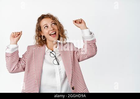 Bonne femme d'affaires en costume sautant et faisant le geste de pompe de poing, en riant et en s'amusant, debout pompé sur fond blanc Banque D'Images
