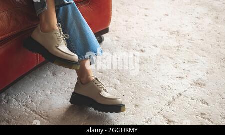 Baskets décontractées et vêtements en denim, jeune fille en studio, assise sur un fauteuil vintage en cuir ancien, fond en béton Banque D'Images