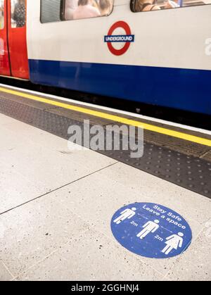 Social distance sur le métro de Londres. Un métro londonien en gare avec un rappel de distance COVID-19 sur le plancher de la plate-forme. Banque D'Images