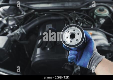 Remplacement du filtre à huile. Le mécanicien d'entretien de moteur de voiture tient un filtre à huile dans sa main contre le fond d'un capot de voiture ouvert Banque D'Images