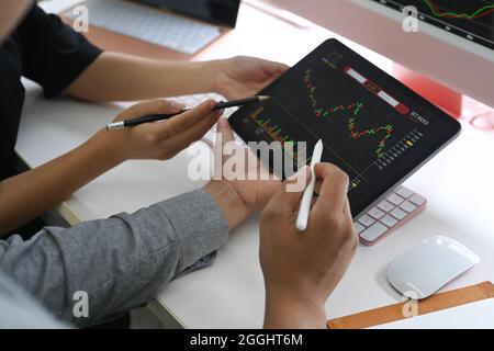 Rogné deux professionnels vérifiant ensemble le marché boursier sur une tablette numérique de bureau. Banque D'Images