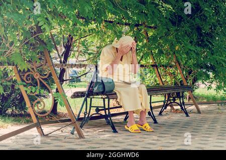 Femme âgée assise sur le banc du parc, lisant un journal. Femme solitaire âgée assise sur un banc dans un parc d'été Banque D'Images