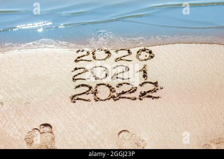 Les chiffres 2021, 2022 sont tirés sur le sable et lavés par la vague, le symbole de la nouvelle année, le changement de l'année Banque D'Images