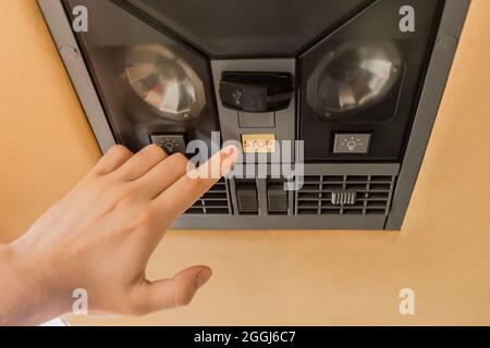 La main du gars pointe son doigt sur le bouton d'arrêt du système de climatisation dans le plafond du bus touristique. Banque D'Images