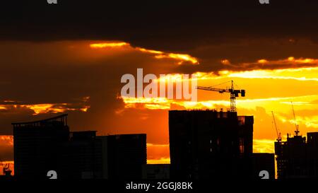 Une grue à tour se levant sur le toit d'un bâtiment sur un chantier de construction. Nuage de tempête spectaculaire sur le ciel de coucher de soleil dans les arrière-plans. Banque D'Images