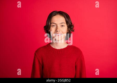 Portrait d'un joli garçon joyeux aux cheveux bruns portant un pull-over tricoté isolé sur fond rouge vif Banque D'Images