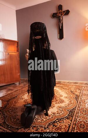 Une femme dans un voile et un costume noirs est agenouillée devant un crucifix Banque D'Images