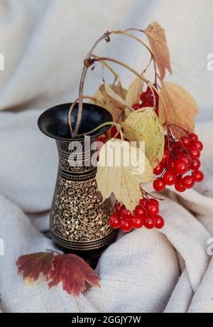 Gros plan des baies de viburnum rouges mûres dans le vase métallique décoratif sur le tissu Banque D'Images