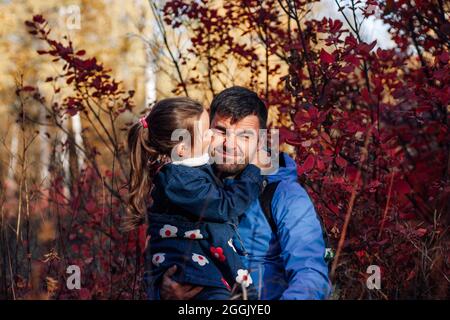 gros plan portrait de famille heureux. petite fille adorable embrasse son père dans une veste bleue à l'automne forêt Banque D'Images